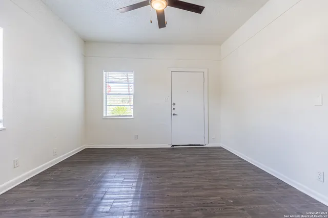 an empty room with wooden floor chandelier fan and windows