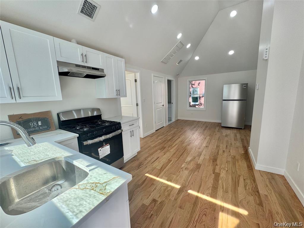 Modern kitchen featuring white cabinetry, stainless steel appliances including a gas range and refrigerator, undermount sink with quartz countertops, recessed lighting, and wood-finish flooring throughout the open-concept living space