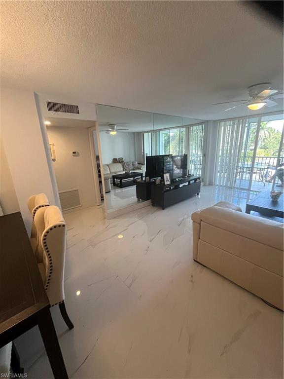 3 Bluebill Avenue, Unit 207 Naples, FL 34108 - Photo 22 of 27 Living room with a ceiling fan, floor to ceiling windows, a textured ceiling, and light marble finish flooring