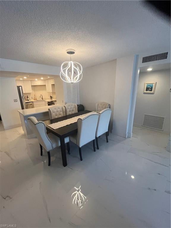3 Bluebill Avenue, Unit 207 Naples, FL 34108 - Photo 10 of 27 Dining space with hanging lights, a textured ceiling, and light marble finish floors