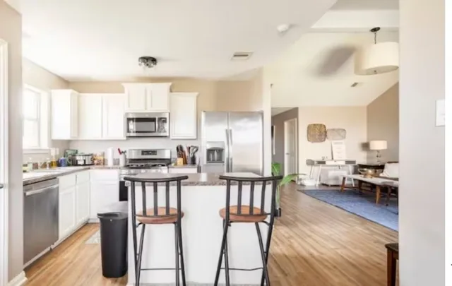 a kitchen with stainless steel appliances kitchen island granite countertop a stove top oven a sink a refrigerator a dining table and chairs with wooden floor