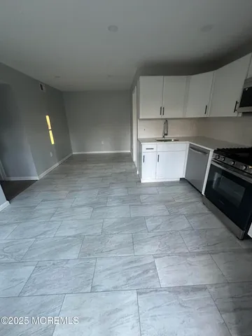 a kitchen with granite countertop a stove a sink and white cabinets