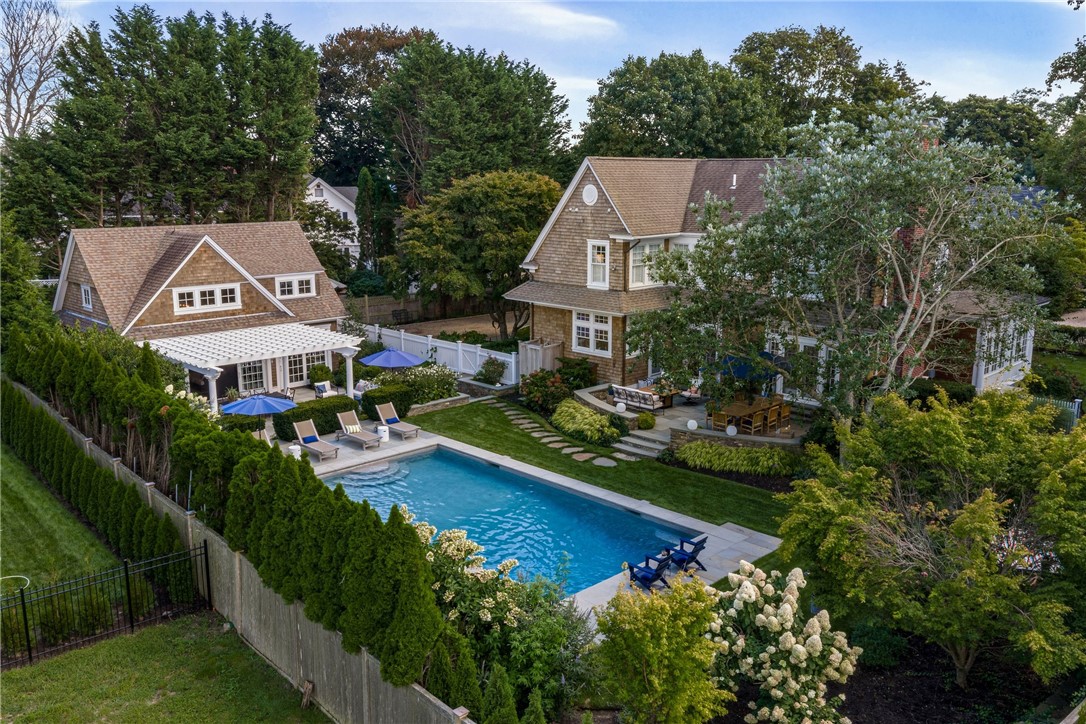 Elevated view of the rear yard showcasing the pool house, patios, and heated gunite pool with retractable cover