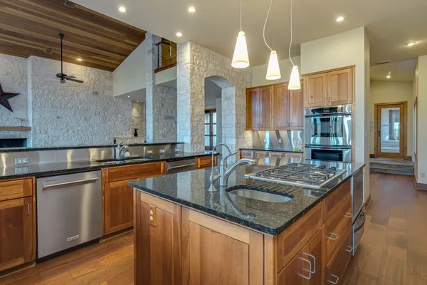a kitchen with stainless steel appliances granite countertop a sink a counter space and a refrigerator