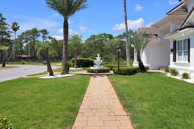 a view of a fountain in front of a house with plants and large trees
