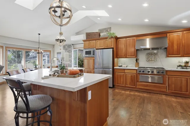 a kitchen with stainless steel appliances granite countertop a refrigerator a stove and a sink with wooden floors