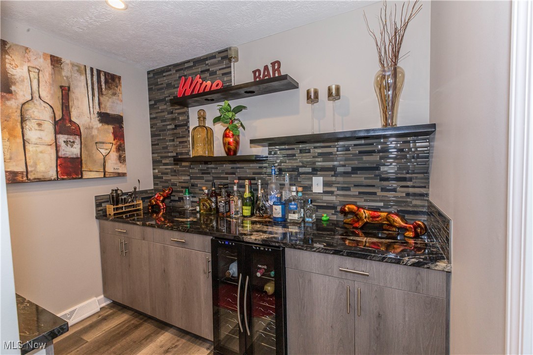 2430 Rockside Road Independence, OH 44131 - Photo 17 of 46 Indoor wet bar featuring open shelves, a textured ceiling, dark stone counters, wine cooler, and decorative backsplash