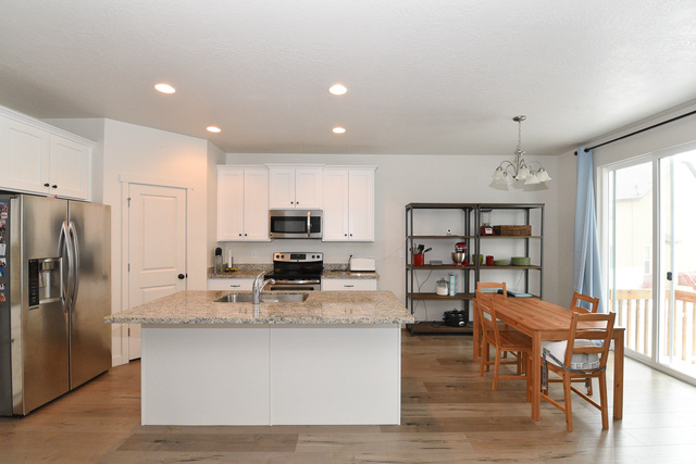 1632 North Apache Road Saratoga Springs, UT 84045 - Photo 5 of 28 Modern kitchen featuring a central island with a light-toned granite countertop, under-mount stainless steel sink, and white cabinetry