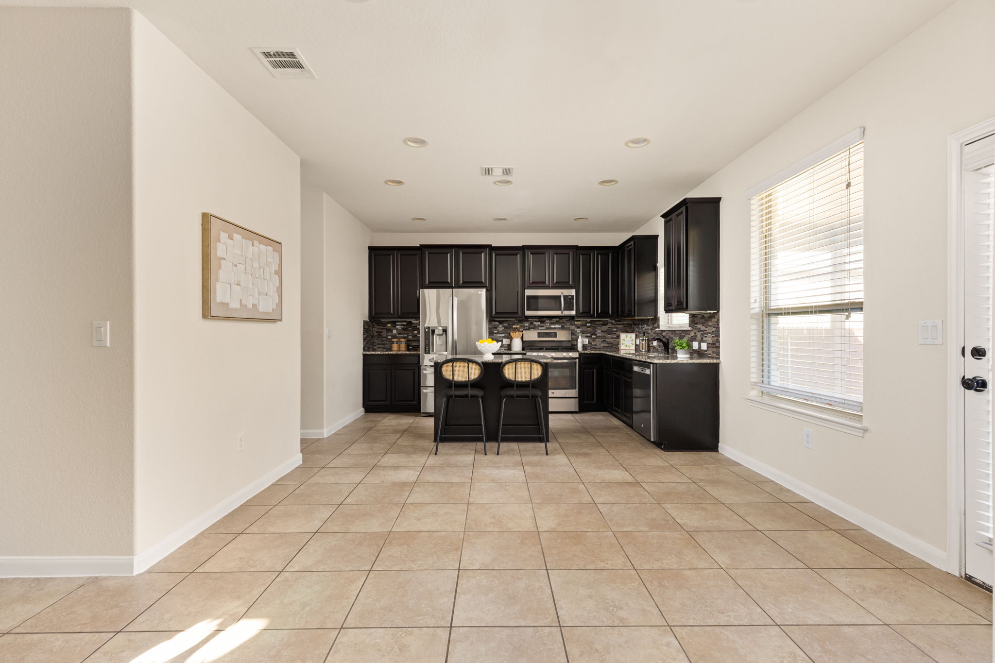 2400 Leonards Pass Leander, TX 78641 - Photo 13 of 40 A contemporary kitchen showcases dark cabinetry, stainless steel appliances, and a central island with seating, all complemented by warm tile flooring.