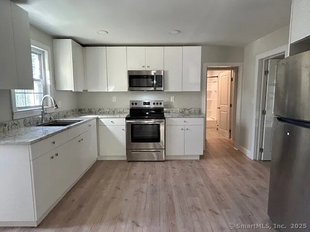 a kitchen with stainless steel appliances granite countertop white cabinets a sink a stove a refrigerator and microwave with wooden floor