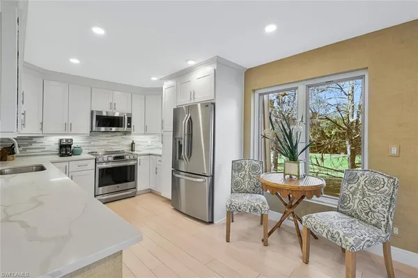 a kitchen with stainless steel appliances granite countertop a refrigerator oven a stove a sink a dining table and chairs with wooden floor