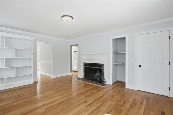 a view of an empty room with wooden floor fireplace and a window