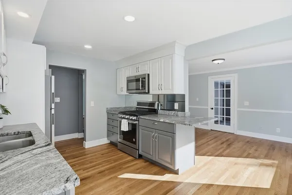 a large kitchen with stainless steel appliances granite countertop a stove top oven a sink dishwasher a dining table and chairs with wooden floor
