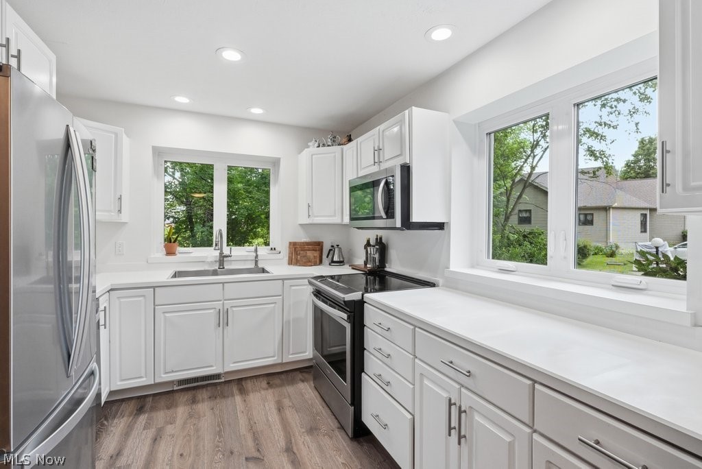 2323 Call Road Stow, OH 44224 - Photo 13 of 42 Kitchen featuring white cabinetry, light-toned countertops, wood-finish flooring, stainless steel appliances, and two large windows