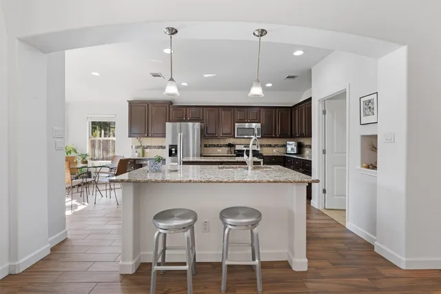 a kitchen with stainless steel appliances kitchen island granite countertop a dining table chairs and a refrigerator