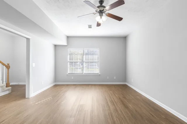 an empty room with wooden floor fan and windows