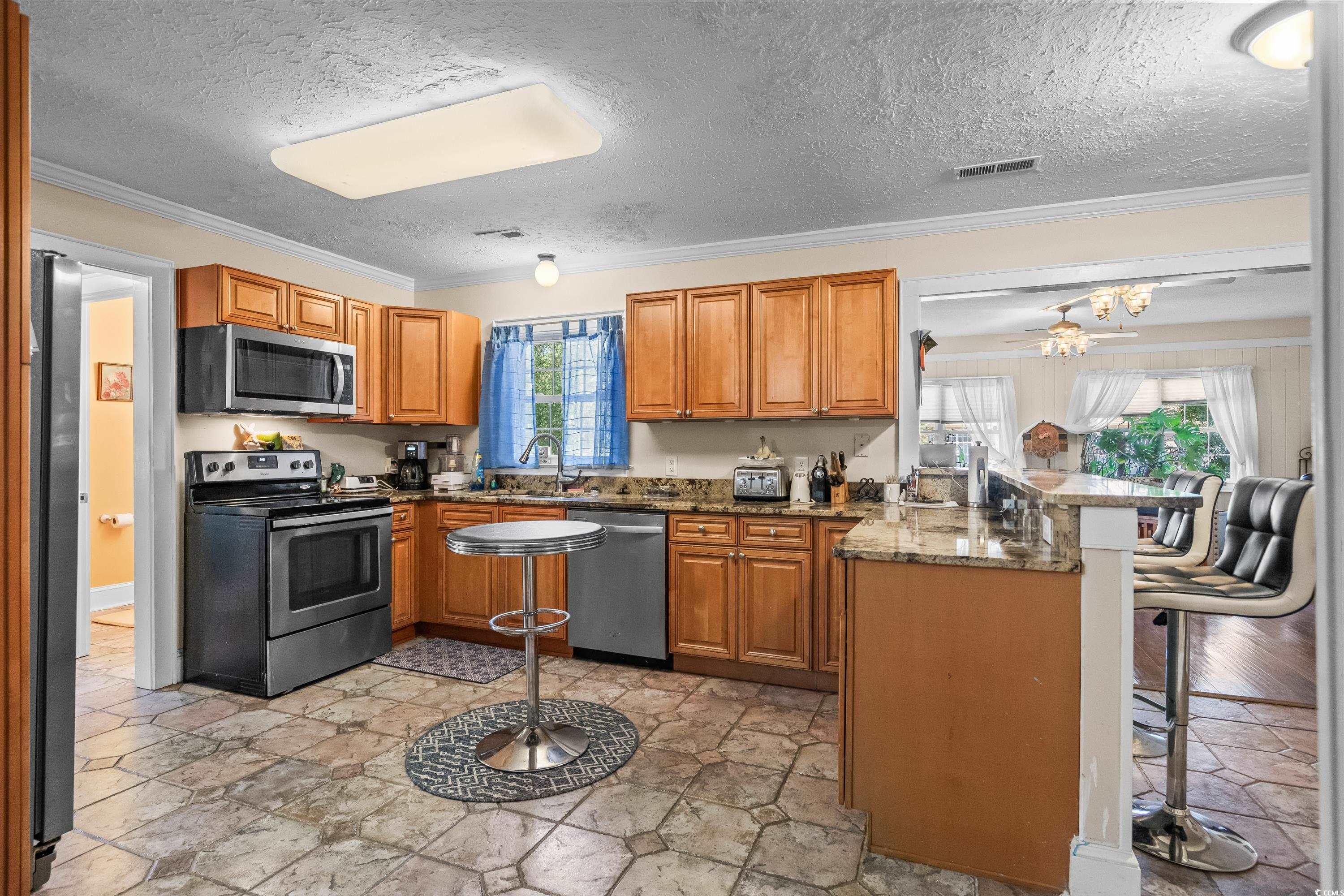 159 Brookgate Drive Myrtle Beach, SC 29579 - Photo 10 of 40 Kitchen with stainless steel appliances, a peninsula, ornamental molding, brown cabinets, and a textured ceiling