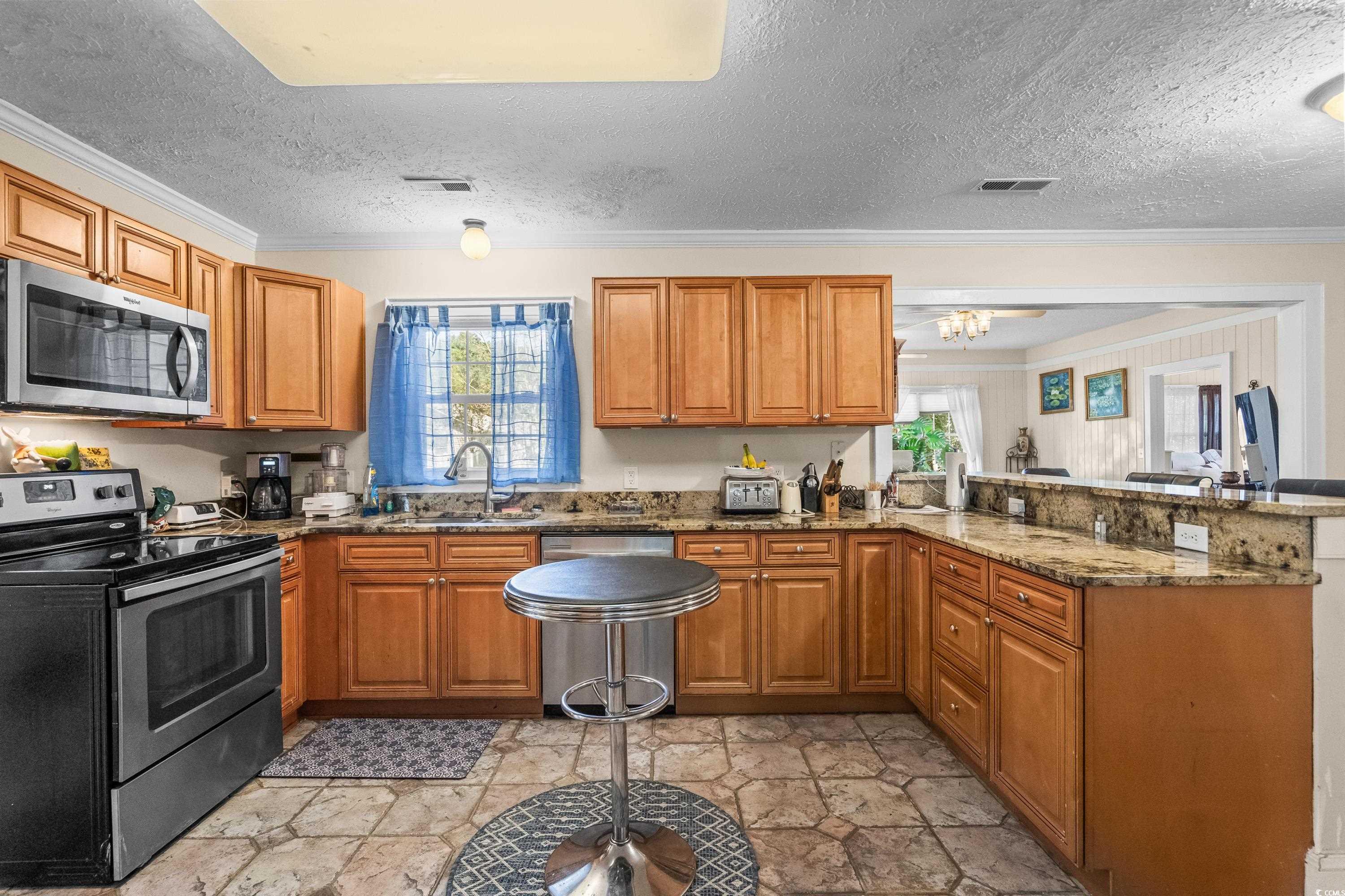159 Brookgate Drive Myrtle Beach, SC 29579 - Photo 11 of 40 Kitchen with stainless steel appliances, a peninsula, brown cabinetry, crown molding, and a textured ceiling
