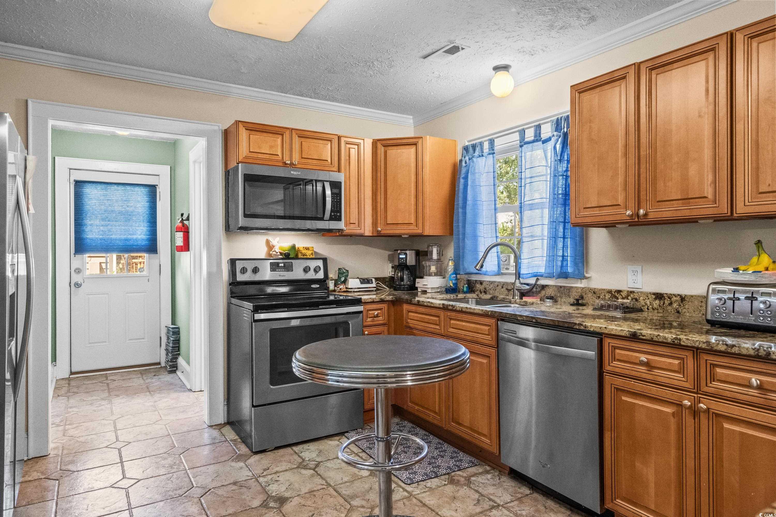 159 Brookgate Drive Myrtle Beach, SC 29579 - Photo 12 of 40 Kitchen with a textured ceiling, stainless steel appliances, ornamental molding, brown cabinets, and dark stone counters