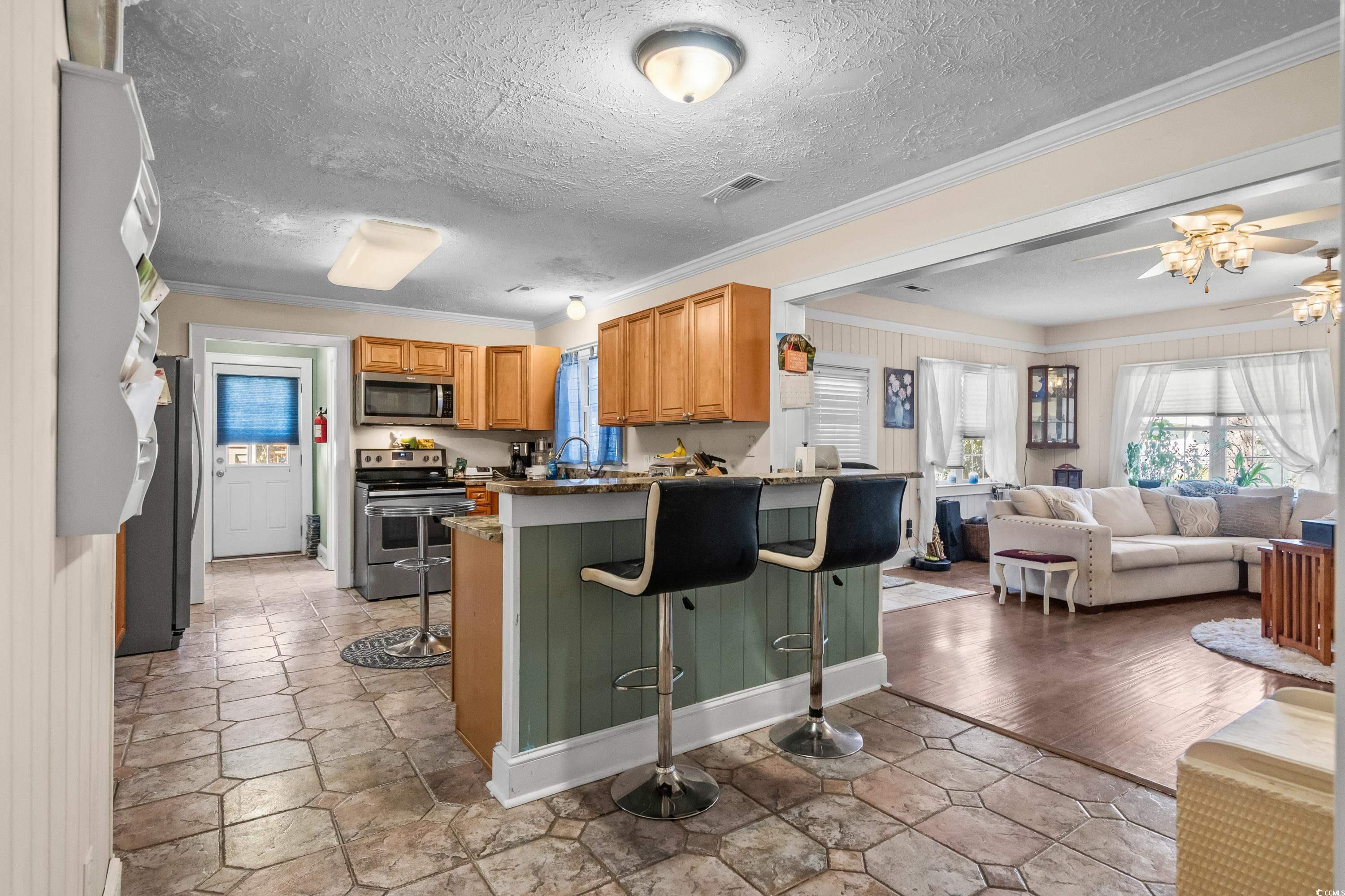159 Brookgate Drive Myrtle Beach, SC 29579 - Photo 40 of 40 Kitchen with a kitchen bar, appliances with stainless steel finishes, ornamental molding, open floor plan, and a textured ceiling