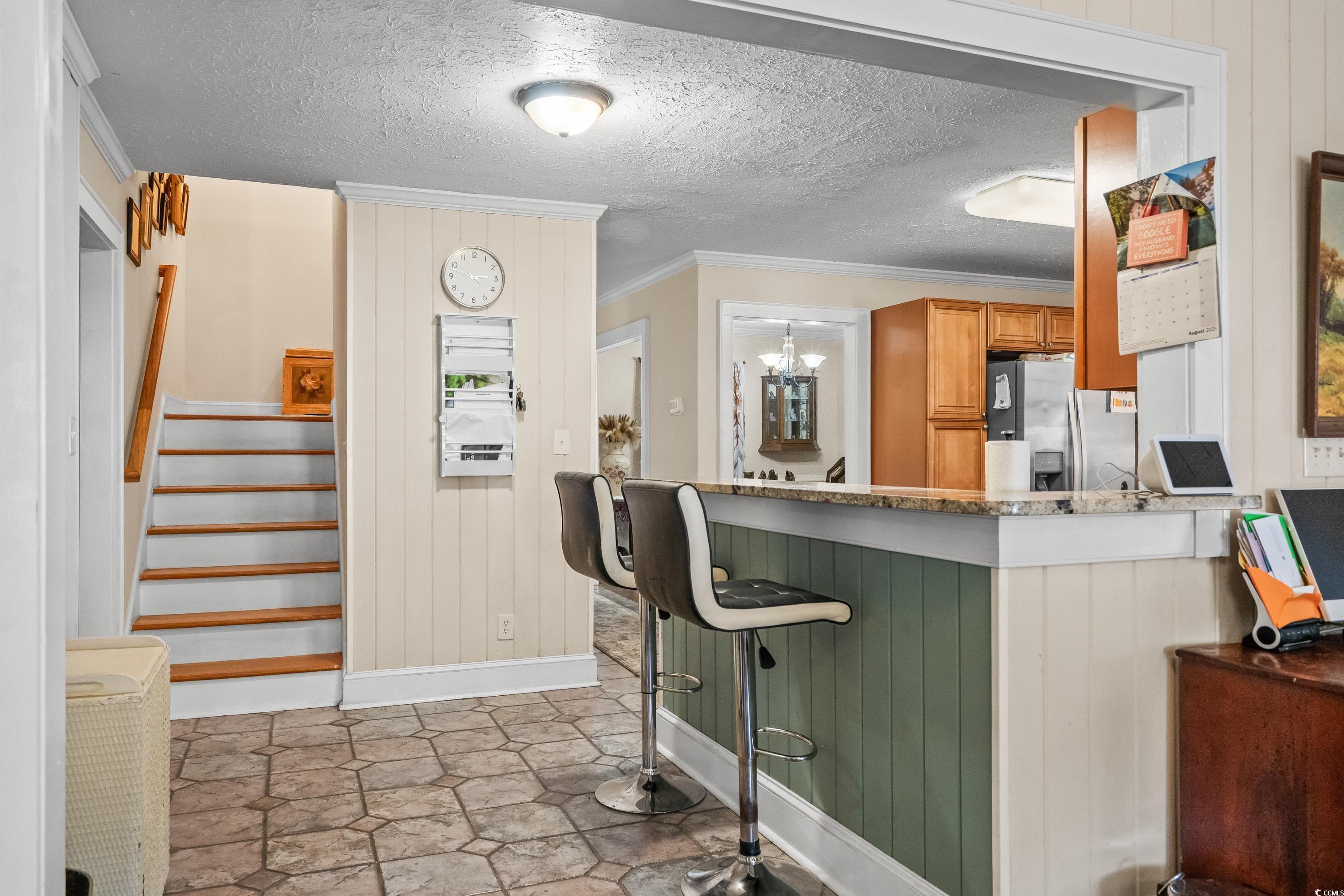 159 Brookgate Drive Myrtle Beach, SC 29579 - Photo 9 of 40 Kitchen with crown molding, wooden walls, a textured ceiling, stainless steel fridge with ice dispenser, and a kitchen bar