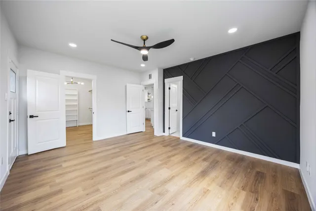 a view of an empty room with wooden floor and a ceiling fan