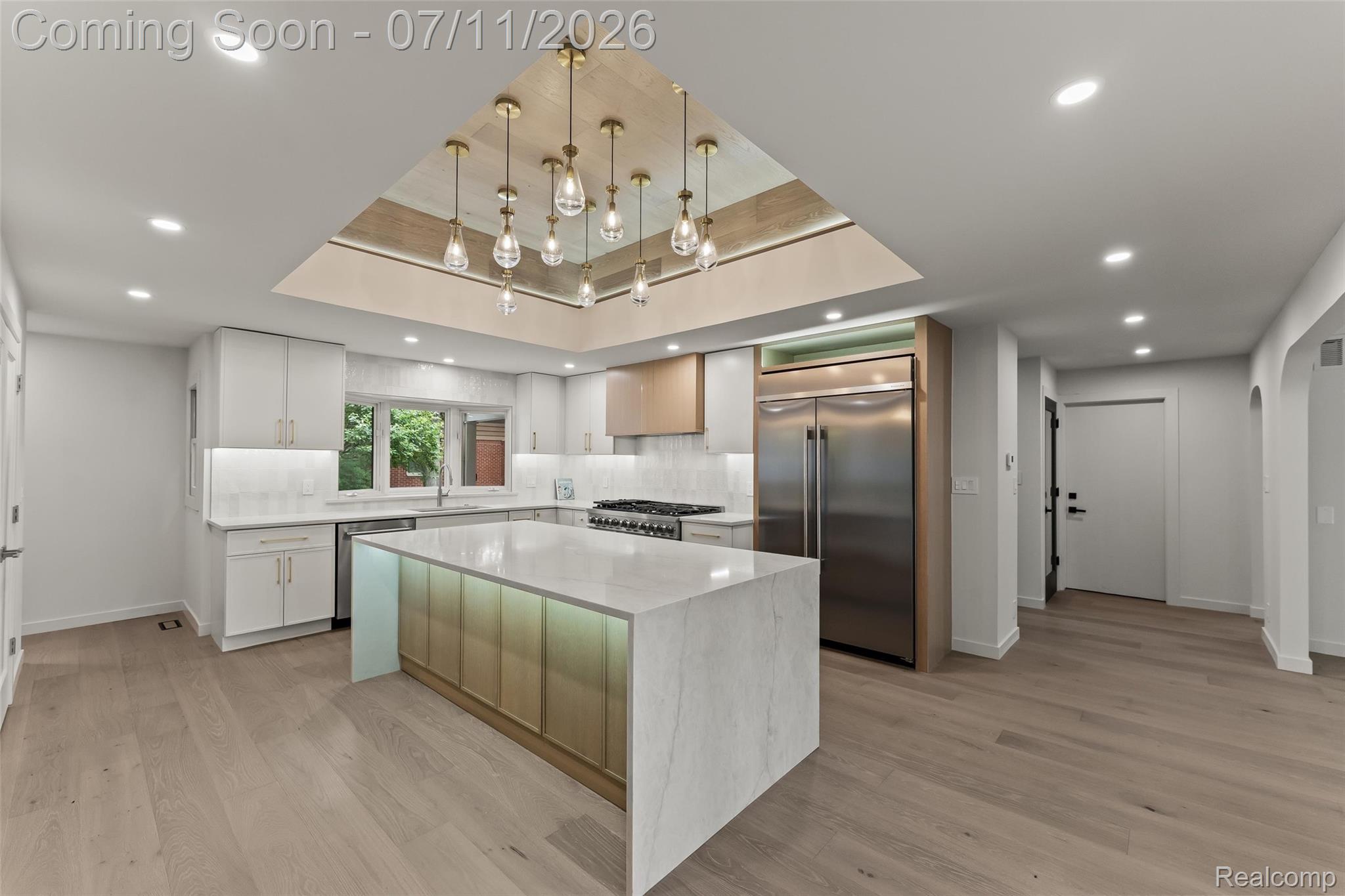 4154 Nearbrook Road Bloomfield Hills, MI 48302 - Photo 14 of 47 Open-concept kitchen featuring an illuminated center island with a waterfall countertop, integrated stainless steel appliances, light wood-finish flooring, white cabinetry with under-cabinet lighting, and a multi-pendant ceiling light fixture