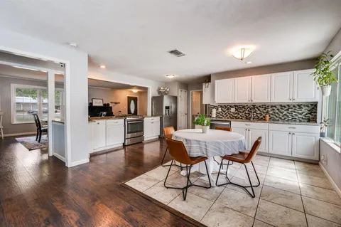 a kitchen with stainless steel appliances kitchen island granite countertop a refrigerator a stove a sink and white cabinets with wooden floor