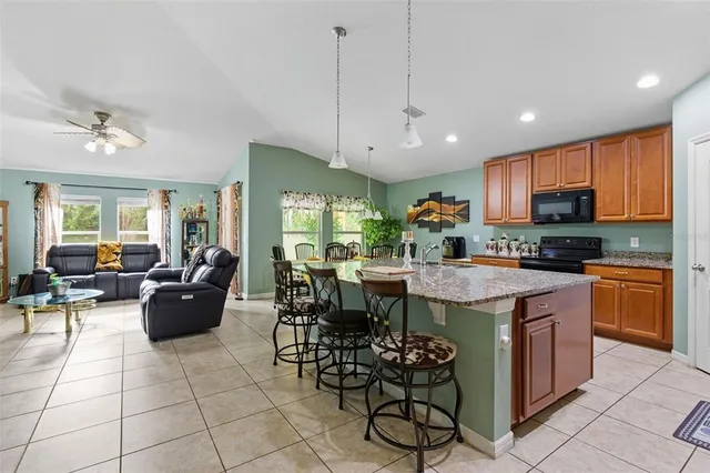 a kitchen with stainless steel appliances granite countertop a stove a sink dishwasher a dining table and chairs with the view of living room