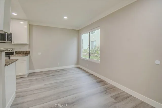 an empty room with wooden floor a kitchen view and windows