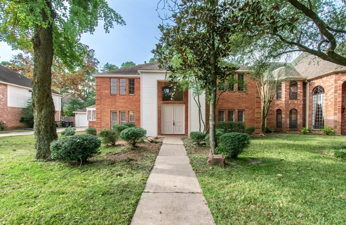 Charming two-story brick home with a welcoming front entrance and large windows. It features a well-maintained front lawn with mature trees and shrubs, creating a pleasant and inviting curb appeal.