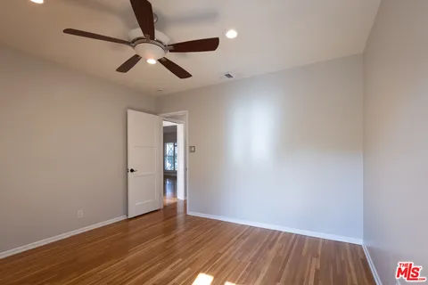 an empty room with wooden floor ceiling fan and window
