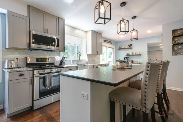 a kitchen with stainless steel appliances a sink a stove a microwave a refrigerator cabinets and living room view