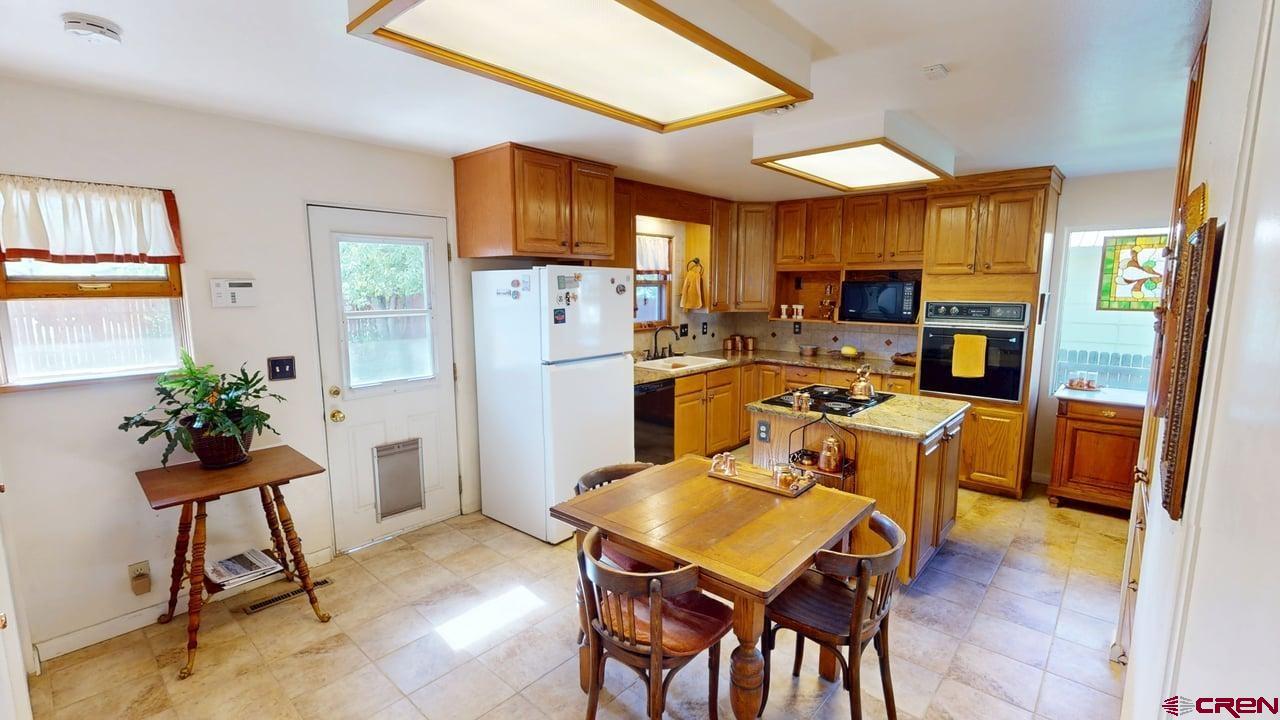 96 El Rio Drive Alamosa, CO 81101 - Photo 5 of 18 a kitchen with stainless steel appliances kitchen island granite countertop a refrigerator a stove a microwave oven a dining table and chairs with wooden floor