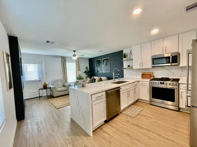 a kitchen with stainless steel appliances a stove top oven a sink dishwasher a refrigerator and white cabinets with wooden floor