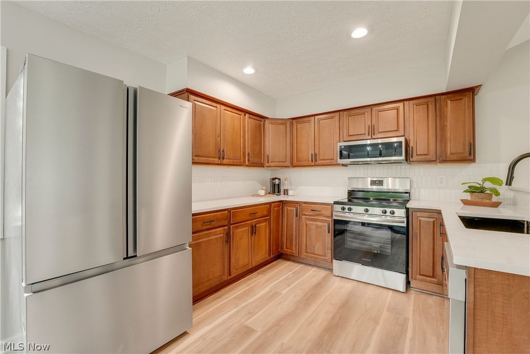 646 Ledge Road Macedonia, OH 44056 - Photo 6 of 28 Kitchen featuring wood cabinetry, stainless steel appliances, white countertops, a white tile backsplash, and light wood-finish flooring
