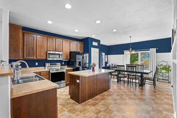 7092 Cherokee Street Eagle Mountain, UT 84005 - Photo 4 of 27 Spacious kitchen featuring warm wood cabinetry, stainless steel appliances, a central island, and durable tile-patterned flooring
