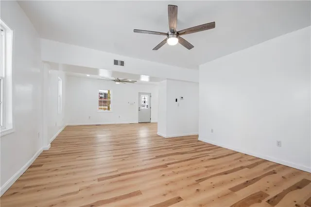 an empty room with wooden floor fan and windows