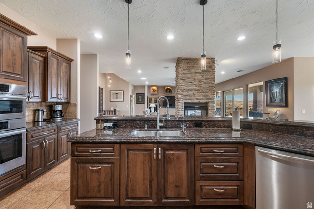 2376 Stone Crest Circle St. George, UT 84790 - Photo 12 of 61 Kitchen featuring dark wood finish cabinetry, stainless steel appliances, dark stone counters, ceiling fan, and a stone fireplace