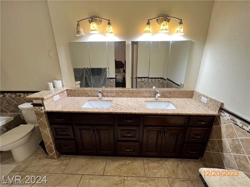9436 Quail Ridge Drive Las Vegas, NV 89134 - Photo 14 of 17 Full bath featuring double vanity, tile walls, a wainscoted wall, and a tub