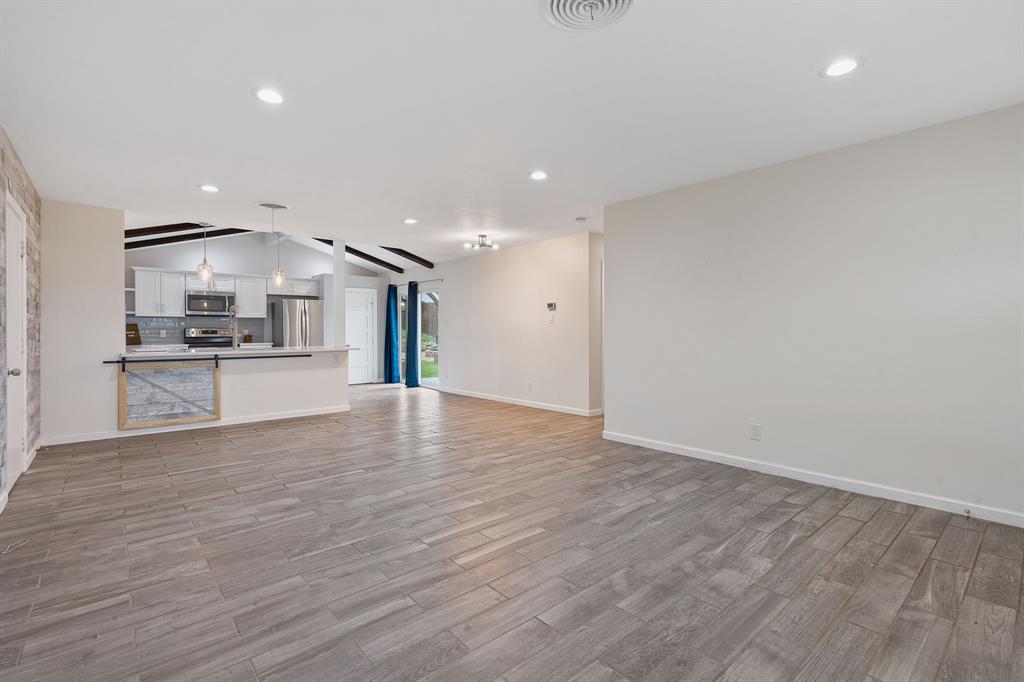 5211 Halmark Drive Austin, TX 78723 - Photo 5 of 27 An open-concept living space with vaulted ceilings and wood-look tile flooring flows into a modern kitchen with stainless steel appliances.