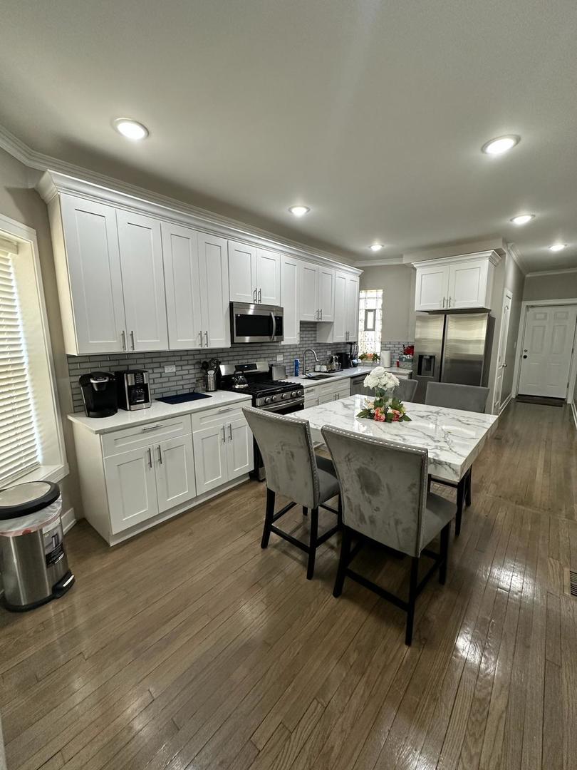 6807 South Calumet Avenue, Unit 1 Chicago, IL 60637 - Photo 4 of 17 a kitchen with a sink dishwasher a stove a microwave oven and a dining table with wooden floor
