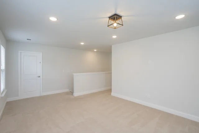 an empty room with a chandelier fan and kitchen view