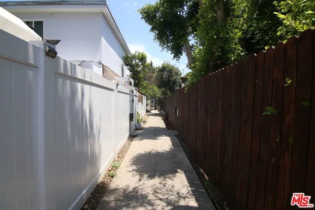 a view of a pathway of a house with wooden fence next to a yard