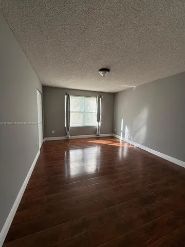 an empty room with wooden floor and windows with curtains