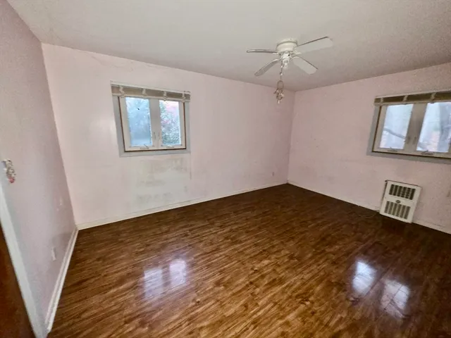 a view of an empty room with wooden floor and a ceiling fan