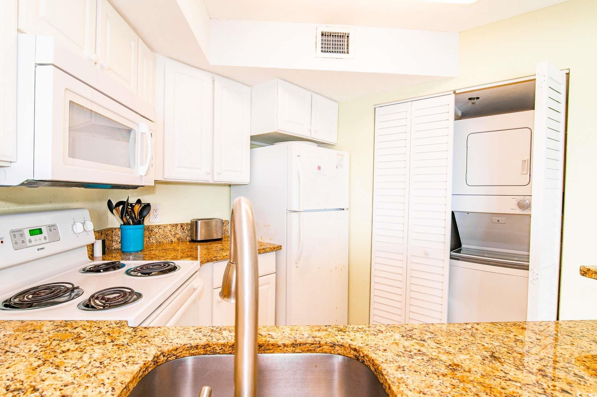 2504 North Ocean Boulevard, Unit 1835 Myrtle Beach, SC 29577 - Photo 11 of 25 Kitchen featuring white appliances, white cabinetry, stacked washer / drying machine, and light stone counters