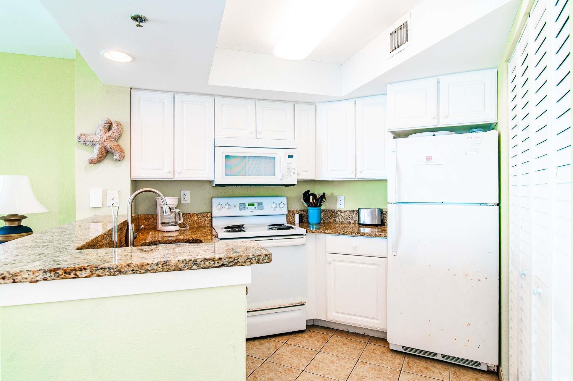 2504 North Ocean Boulevard, Unit 1835 Myrtle Beach, SC 29577 - Photo 9 of 25 Kitchen featuring white appliances, white cabinets, a peninsula, light stone countertops, and light tile patterned floors