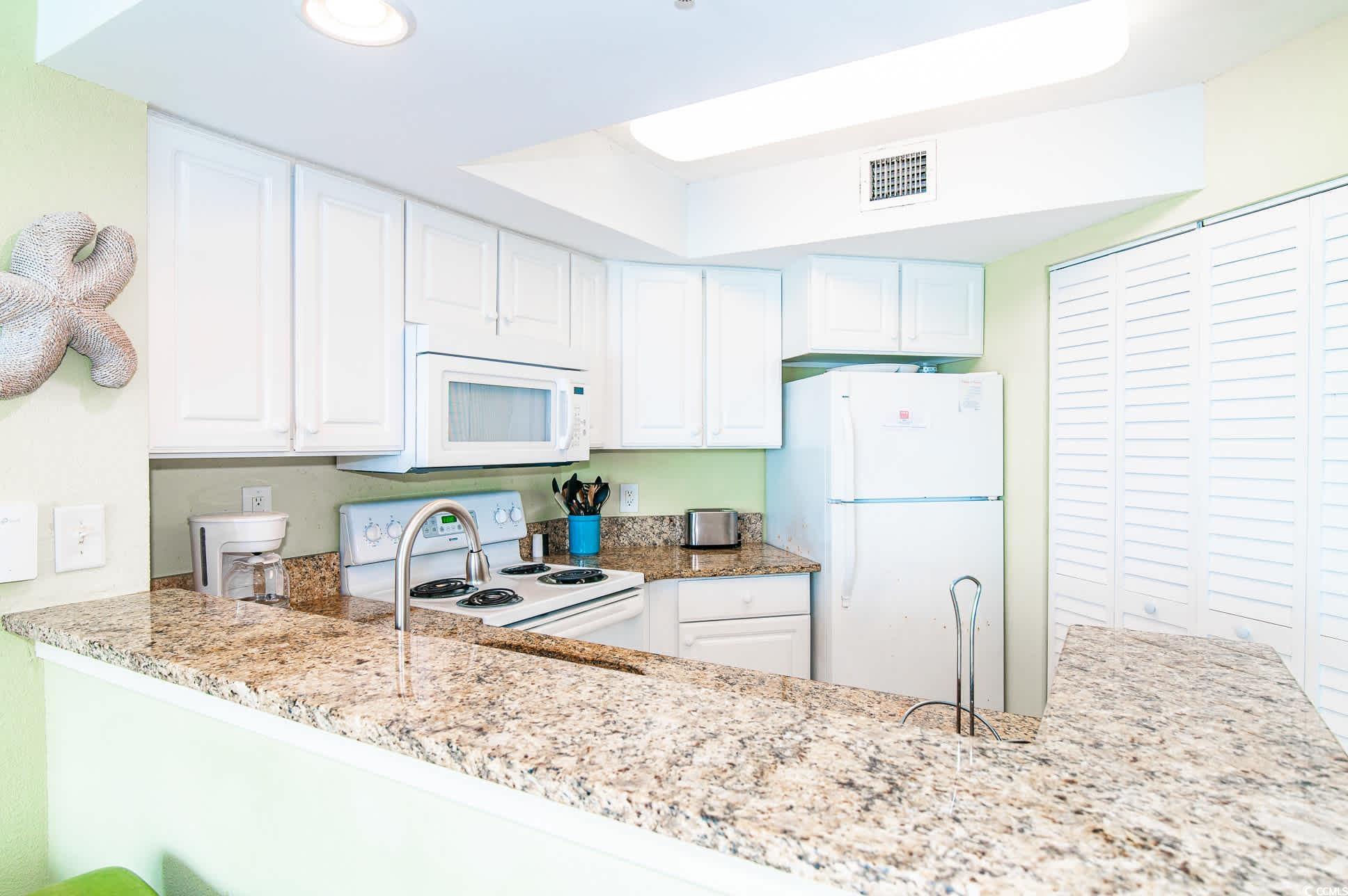 2504 North Ocean Boulevard, Unit 1835 Myrtle Beach, SC 29577 - Photo 10 of 25 Kitchen with white cabinetry, white appliances, light stone countertops, and a peninsula