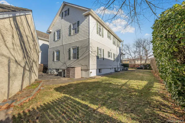 a view of a white house next to a yard with large trees